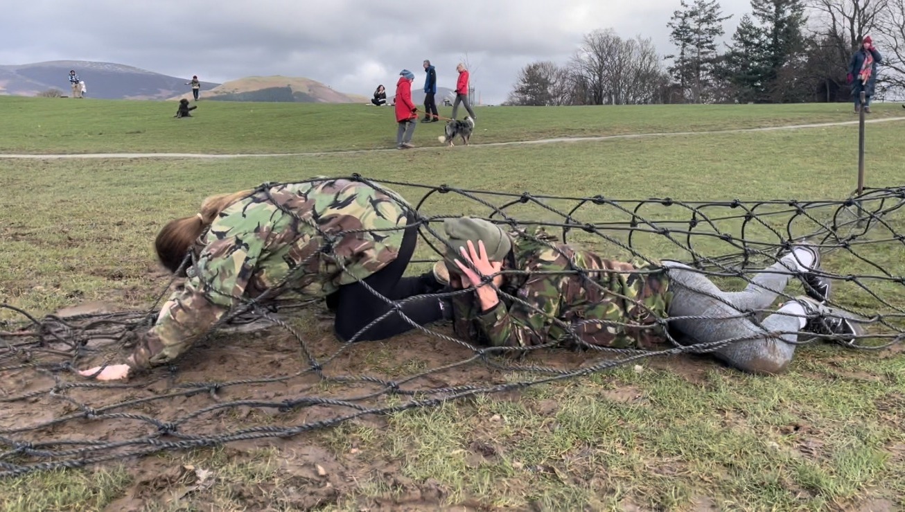 Two women crawling under a cargo net