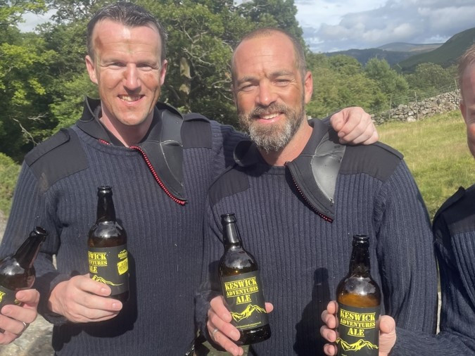 A group standing outdoors enjoying bottles of Keswick Adventures Ale.