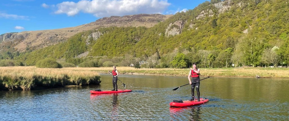 Two people on paddleboards in a river in Borrowdale