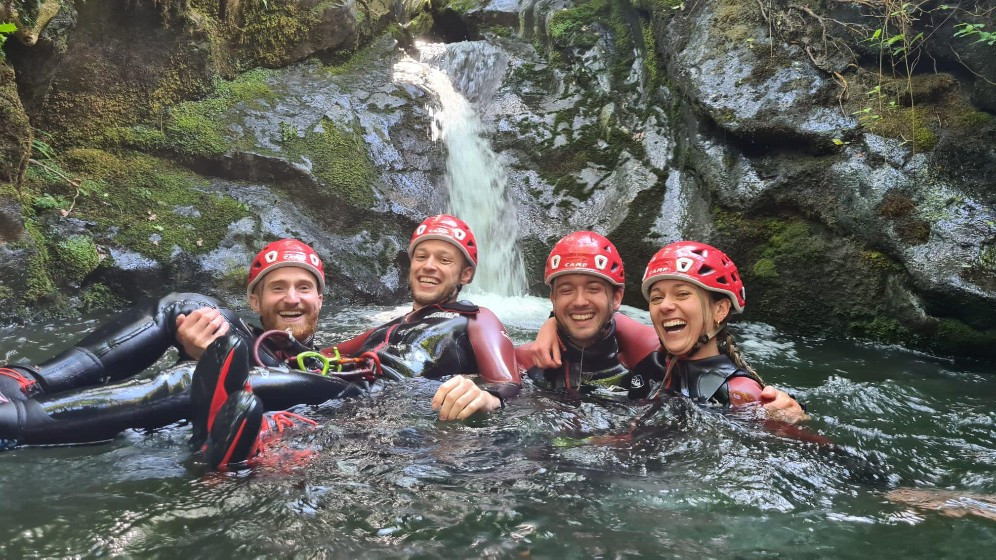 Group of smiling people in front of a small waterfall in a river pool
